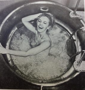 Black and white photo of lady in a circular metal bath enjoying the bubbles