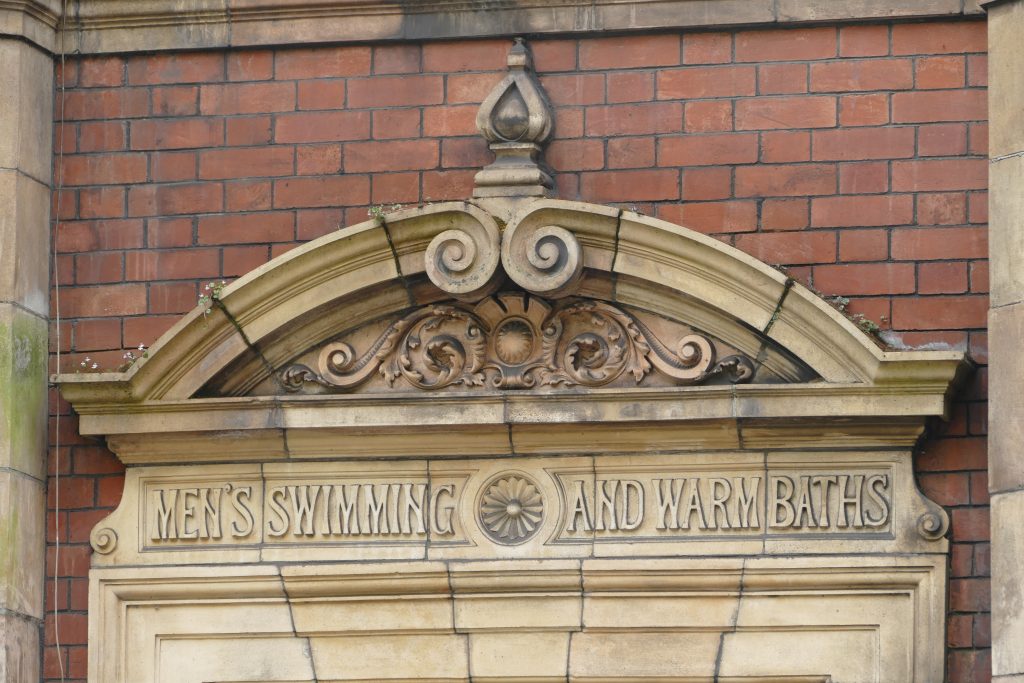 Photo of stone fascia over the men’s entrance, with lettering “Men’s swimming andwarm baths”